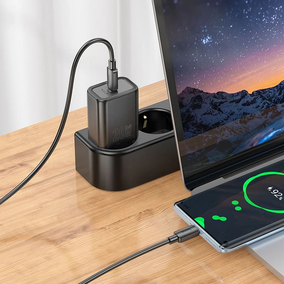 A black dual-device wireless charging dock sits on a wooden desk, with one device charging a laptop and the other charging a smartphone. The charger has a power rating of 20W visible on the side.